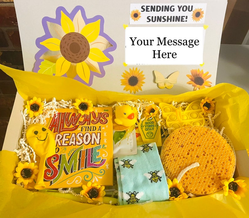 May include: A yellow gift box filled with yellow themed items, including a yellow smiley face balloon, a yellow bath sponge, a yellow pop-it toy, a yellow rubber duck, and a card with the text "Always find a reason to smile".