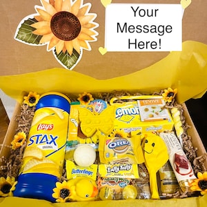 May include: A yellow gift box filled with various yellow themed snacks and toys. The box is decorated with a sunflower and the text "Your Message Here!"  The snacks include Lay's Stax crisps, Oreo cookies, Laffy Taffy, Milky Way, and Butterfinger. The toys include a yellow rubber duck, a yellow pop-it, and a yellow balloon.