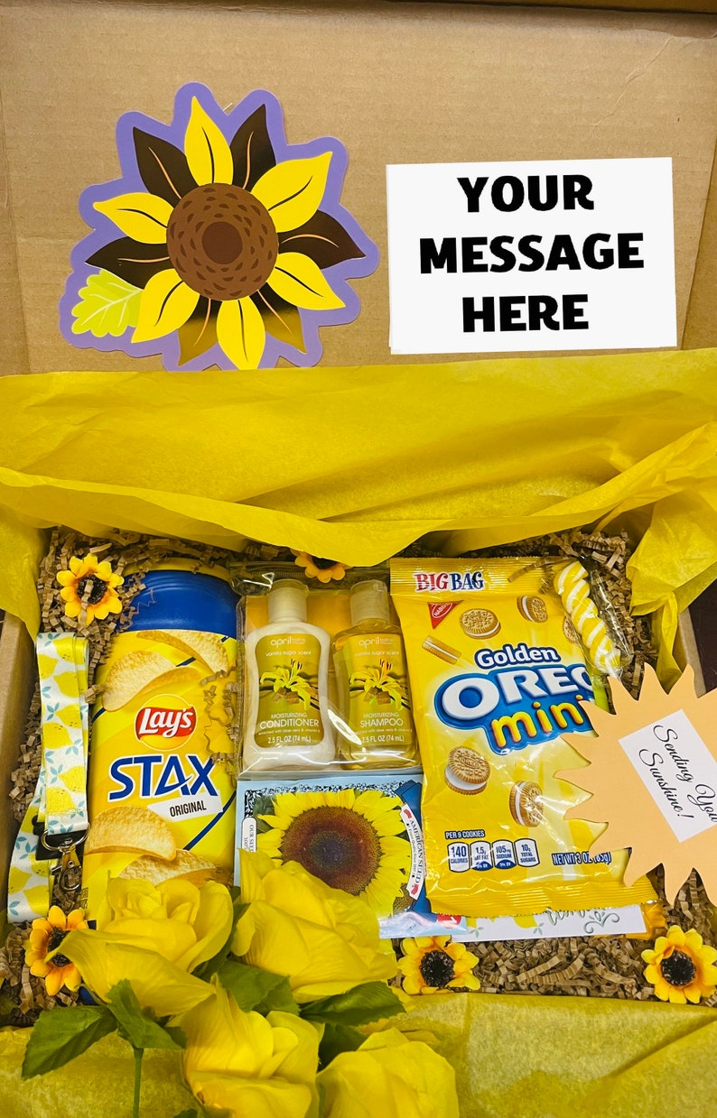 May include: A yellow gift box filled with various items, including a bag of Lay's Stax potato chips, two bottles of hair care products, a bag of Oreo Mini cookies, and a yellow sunflower. The box is decorated with a yellow sunflower and a note that says "Sending You Sunshine!"