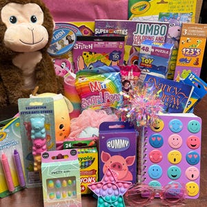 May include: A collection of children's items including a brown plush monkey, a spiral notebook with colorful smiley faces, a star-shaped pop-it toy, a Rummy card game, Crayola crayons, Mini Swirl Pops, a Nancy Drew book, and various small toys.