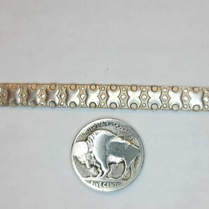 May include: A silver chain bracelet with a repeating geometric pattern. The chain is about 2 inches long and is shown next to a US nickel for scale.