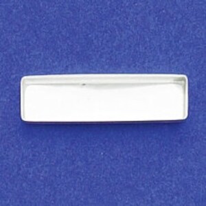 May include: A rectangular, silver-colored metal tray with a shallow, white interior. The tray is empty and sits against a solid blue background. The tray's edges are slightly rounded.