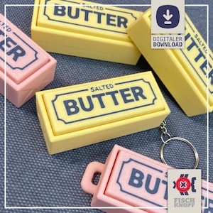 May include: Several rectangular butter-shaped keychains in pastel yellow and light pink. Each piece features a dark blue border and the text "SALTED BUTTER" printed on the top surface. One pink keychain includes a metal ring attachment.