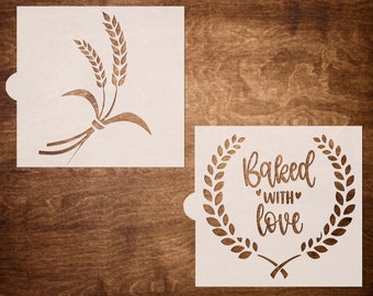 May include: Two white stencils for baking. One stencil features a wheat stalk design. The other stencil features a wreath with the text "Baked with love".