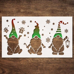 May include: A wooden cutout depicting three gnomes with green hats and brown bodies. The gnomes are set against a white background with snowflakes, stars, and gift boxes. One gnome holds a lantern, another a candy cane.