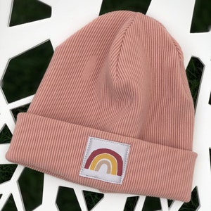 May include: A pink knitted beanie with a rainbow patch. The rainbow is in shades of red, orange, yellow, and brown.