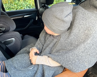 May include: A grey wool-like poncho worn over a long-sleeved shirt, paired with a matching grey knit beanie. The garment features a front pocket and covers the upper body, while blue and tan striped socks are visible on the lower legs.