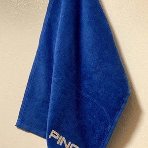 May include: A blue golf towel with the word "PING" embroidered in silver thread.