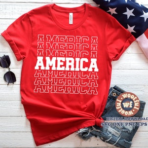 May include: Red t-shirt with a white graphic design that says "AMERICA" in a stacked, retro style. The shirt is folded and displayed on a white wooden surface.
