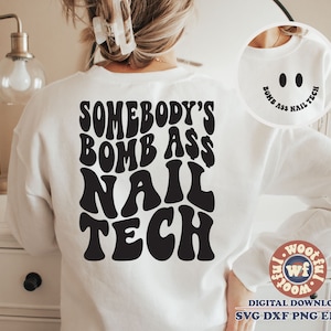 Op de afbeelding: Wit sweatshirt met zwarte tekst die "Somebody's Bomb Ass Nail Tech" luidt in een retro lettertype. De tekst is gecentreerd op de achterkant van het sweatshirt.