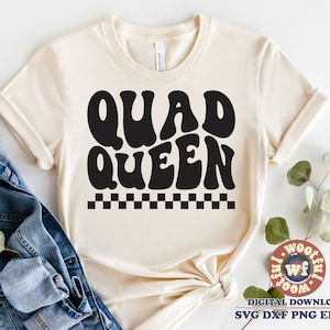 May include: A beige t-shirt with a black graphic that says "QUAD QUEEN" in a retro font with a black and white chequered pattern underneath.