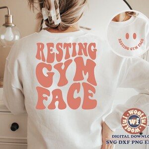May include: White sweatshirt with the text "RESTING GYM FACE" in pink retro font. The text is centred on the sweatshirt.