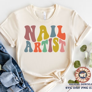 May include: A beige t-shirt with the text "NAIL ARTIST" in colorful retro-style lettering.