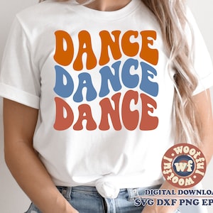 Puede incluir: Una camiseta blanca con las palabras "Dance Dance Dance" en una fuente retro y colorida. Las palabras están apiladas una encima de la otra, con la palabra superior en naranja, la palabra del medio en azul y la palabra inferior en naranja.