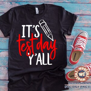 May include: Black t-shirt with white text that says "It's test day y'all" with a white pencil drawing above the text.