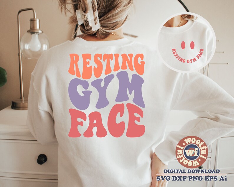 May include: White sweatshirt featuring the text "RESTING GYM FACE" in colourful, retro-style lettering. The text is in a large font and is centred on the sweatshirt. The sweatshirt is being worn by a person, but the person's face is not visible.