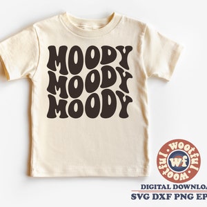 May include: A cream colored t-shirt with the word "MOODY" repeated three times in a retro, black, wavy font.