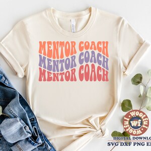 May include: A beige t-shirt with the text "MENTOR COACH" repeated three times in a retro, wavy font. The text is in shades of pink, orange, and purple.