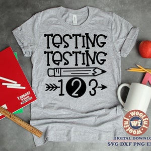 Puede incluir: Camiseta gris con texto negro que dice "Testing Testing 1 2 3" con un gráfico de lápiz blanco y negro y una flecha.