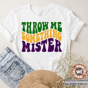 May include: White t-shirt with the text "Throw Me Something Mister" in green, yellow, and purple retro font.