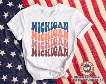May include: White t-shirt with a stacked design of the word "Michigan" in a retro, wavy font. Each word is a different color, starting with blue and transitioning to red.