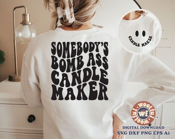 May include: White sweatshirt with black text that reads "Somebody's Bomb Ass Candle Maker" in a retro font.