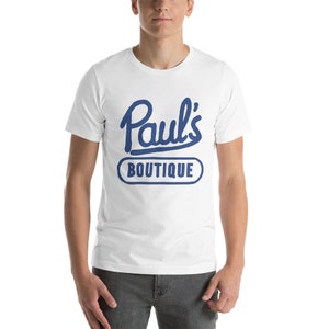 Könnte beinhalten: Weißes T-Shirt mit einer blauen Grafik, auf der "Paul's Boutique" in einer Vintage-Schriftart steht.