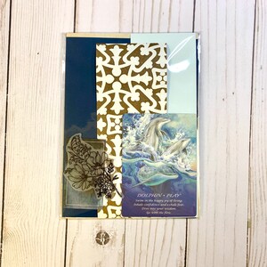 May include: A card with a blue background and a gold patterned design. The card features a picture of dolphins jumping out of the water. The text on the card reads "DOLPHIN PLAY Swim in the happy joy of living. Inhale confidence and exhale fear. Dive into your wisdom. Go with the flow."
