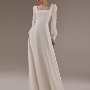 May include: A white wedding dress with long sleeves and a square neckline. The dress has a fitted bodice and a flowing skirt.