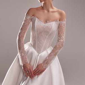 K&ouml;nnte beinhalten: Wei&szlig;es Brautkleid mit Satinrock und Spitzenoberteil. Die schulterfreien &Auml;rmel sind aus zarter Spitze gefertigt. Das Kleid hat ein klassisches, elegantes Design, perfekt f&uuml;r eine Hochzeit.