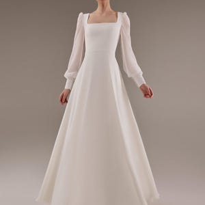 May include: A white wedding dress with a square neckline and long sleeves. The dress has a fitted bodice and a flowing skirt.