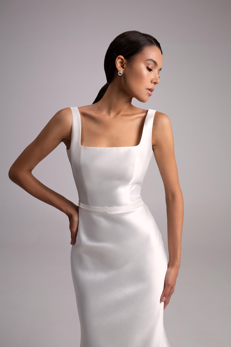 May include: A white sleeveless dress with a square neckline and a fitted silhouette. The dress has a simple design and a smooth, satin-like texture.