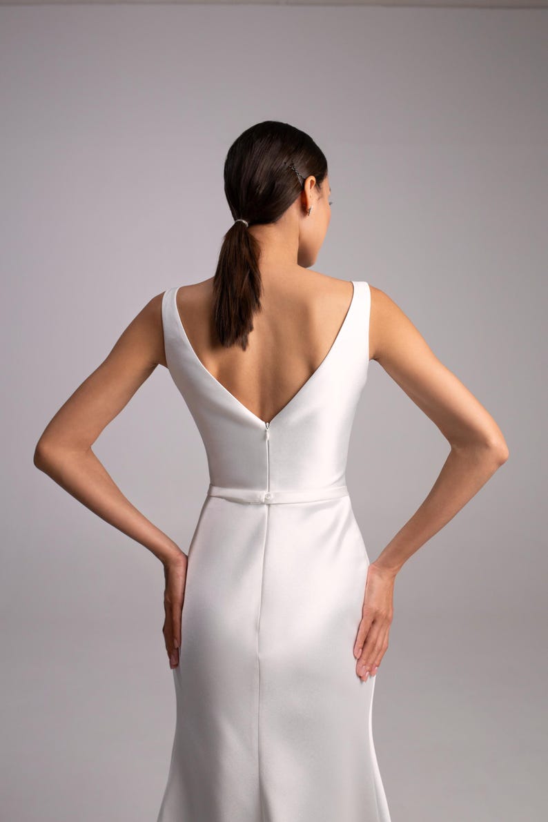 May include: A white sleeveless satin wedding dress with a deep V-neckline and a fitted skirt.