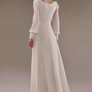 May include: A white long-sleeved maxi dress with a scoop neckline and a fitted bodice. The dress has a flowing skirt and a back zipper closure.