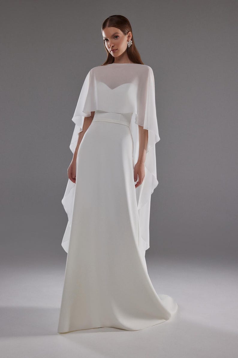 A white bridal chiffon cape. The cape is made of a sheer fabric and drapes over the shoulders, creating a soft, ethereal look.
