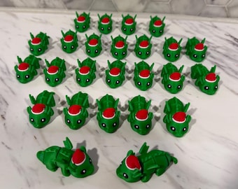 May include: A collection of green dragon figurines, each with a red and white Santa hat. The dragons have detailed features and are arranged on a light-colored surface. The figurines are likely decorative items or toys.