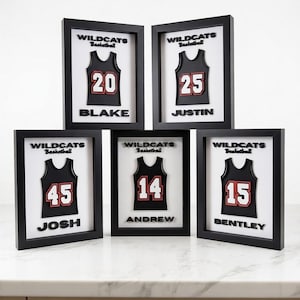 May include: Five framed basketball jersey art pieces. Each black frame features a jersey design with a number and name. The jerseys are black with red accents. The text "WILDCATS Basketball" is above each jersey.
