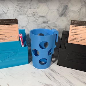 May include: Three 3D-printed organizers in blue, black, and a blue cup with circular cutouts. The organizers have slots for pens and a USPS missed delivery notice. The blue organizer has the USPS logo.