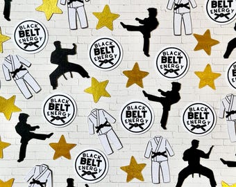 Puede incluir: Un patrón de uniformes de karate blancos con cinturones negros, siluetas de karate negras, estrellas doradas y pegatinas circulares con el texto "BLACK BELT ENERGY" sobre un fondo de ladrillos blancos.