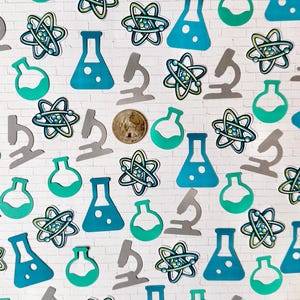 Puede incluir: Una colecci&oacute;n de recortes de papel con tem&aacute;tica cient&iacute;fica, que incluyen vasos de precipitados, modelos at&oacute;micos y microscopios, en tonos de verde azulado, verde y gris. Los recortes est&aacute;n esparcidos sobre un fondo de ladrillos blancos.