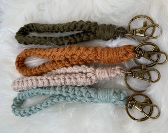 May include: Four crocheted keychains in different colors: olive green, orange, beige, and light blue. Each keychain has a gold metal key ring.