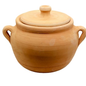 May include: A terracotta cooking pot with a lid and two handles. The pot is a light brown colour and appears to be made of clay. The lid has a small knob on top for easy removal. The pot is round and has a rustic appearance.