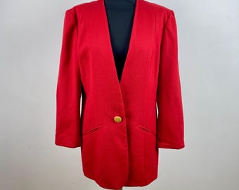 Puede incluir: Un blazer rojo vibrante con un solo botón dorado. El blazer presenta una solapa con muescas clásica y dos bolsillos delanteros. La prenda se exhibe en un maniquí, mostrando su silueta entallada y su diseño estructurado.