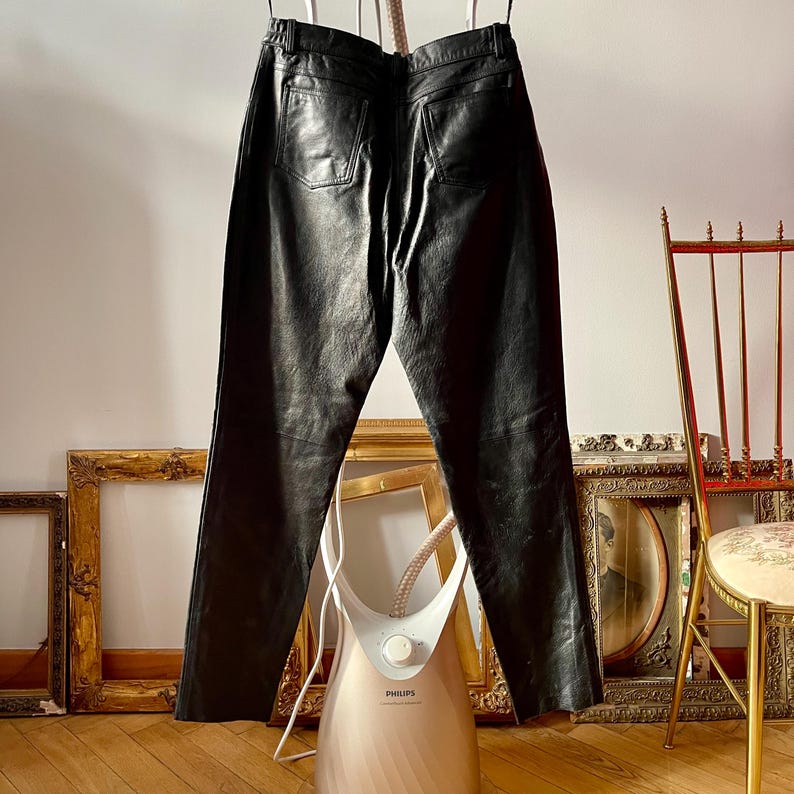 Peut inclure: Pantalon en cuir noir suspendu &agrave; un cintre. Le pantalon a une jambe droite et une fermeture &eacute;clair. Le pantalon est suspendu devant un mur blanc.