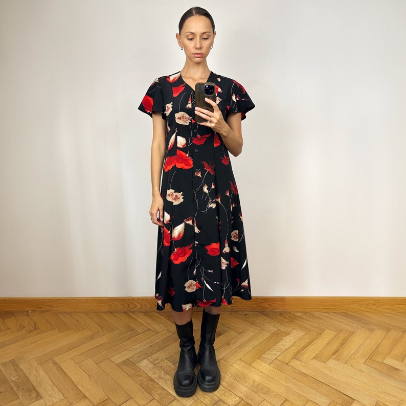 Peut inclure: Une femme portant une robe midi noire &agrave; imprim&eacute; floral rouge et des bottines noires &agrave; la cheville.