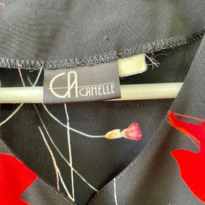 Peut inclure: Gros plan sur un chemisier &agrave; imprim&eacute; floral noir et rouge avec une &eacute;tiquette blanche sur laquelle est inscrit "CA CAMELLE".