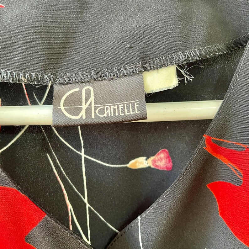 Peut inclure: Gros plan sur un chemisier &agrave; imprim&eacute; floral noir et rouge avec une &eacute;tiquette blanche sur laquelle est inscrit "CA CAMELLE".