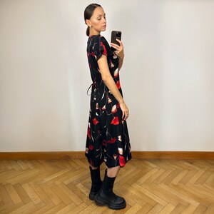 Peut inclure: Une robe midi noire &agrave; imprim&eacute; floral rouge et blanc. La robe a un col en V et des manches courtes. Le mannequin porte des bottes noires.