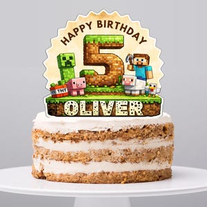 Può includere: Una torta a strati con una base di glassa bianca, sormontata da un cake topper a tema Minecraft. Il topper presenta le parole "Happy Birthday" e "5", insieme ai personaggi di Minecraft e al nome "Oliver".