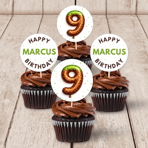 Può includere: Quattro cupcake al cioccolato con glassa al cioccolato e decorazioni. Le decorazioni sono cerchi bianchi con la scritta "HAPPY MARCUS BIRTHDAY" in verde e marrone. Un decoro presenta un palloncino marrone con il numero 9.